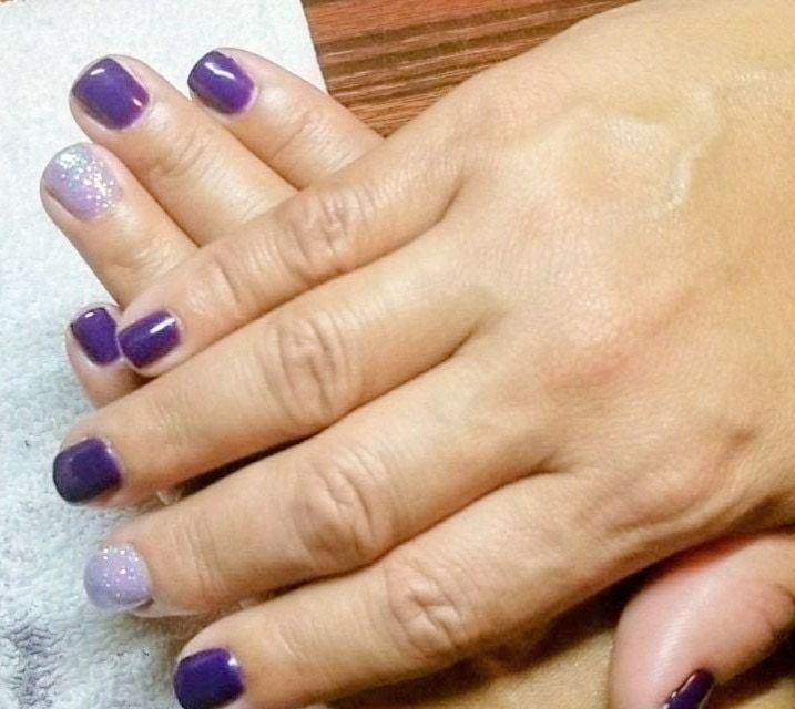 Hands with deep purple nails and two lilac glitter accent nails, done with the dip-powder technique.